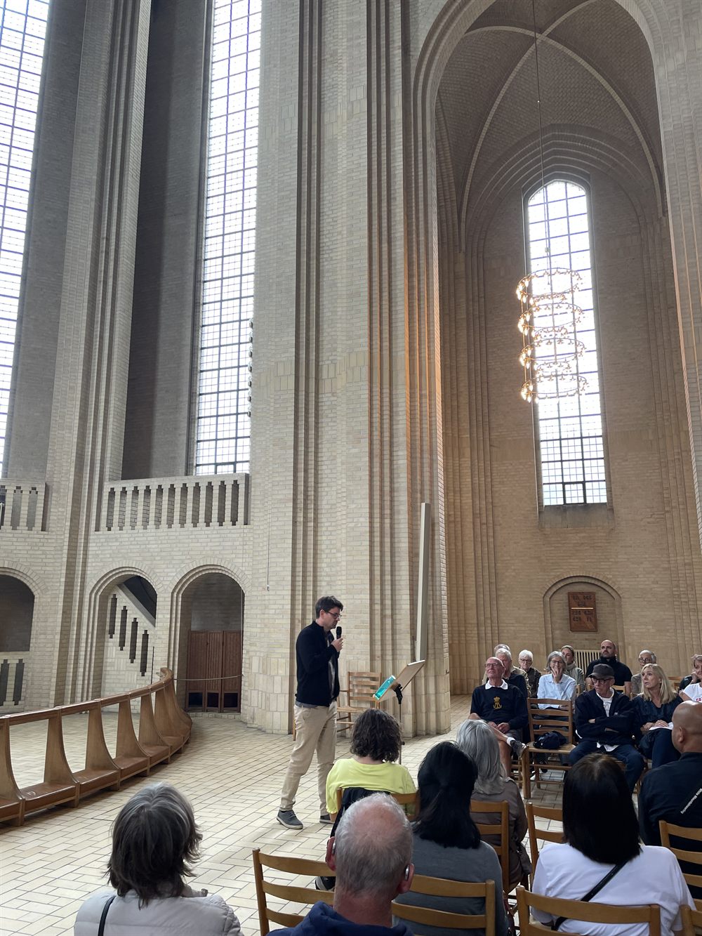 Erik Bork speaking with a microphone to a seated audience inside a tall brick church